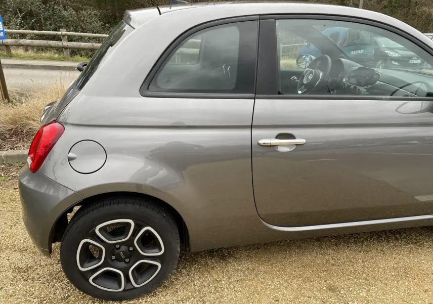 Vue latérale gauche d'une FIAT 500 Hybrid gris foncé, mettant en valeur la roue avant et la poignée de porte chromée.
