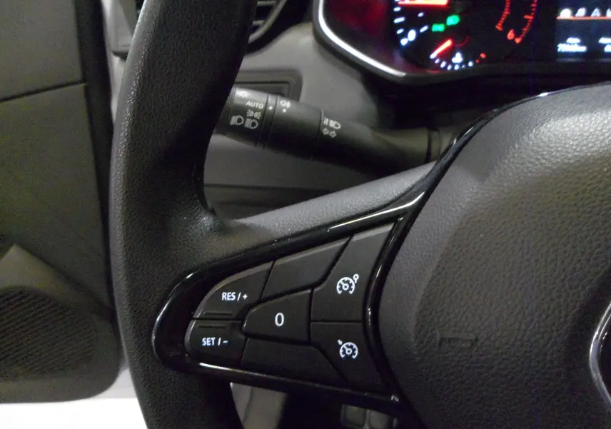 Gros plan sur les commandes de régulateur de vitesse au volant noir d'une Renault Clio V blanche Glacier de 2020.