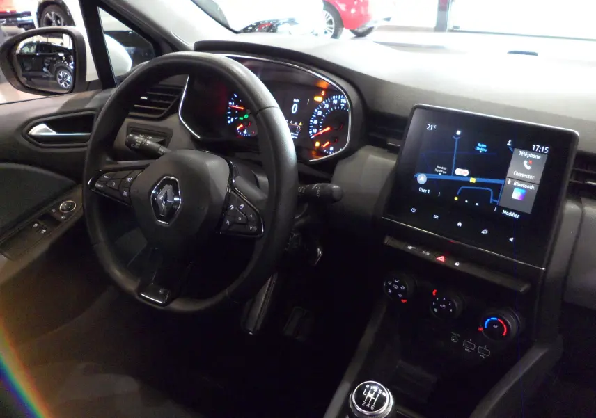 Intérieur de la Renault Clio V blanche, vue côté conducteur sur le volant, tableau de bord et écran tactile central.