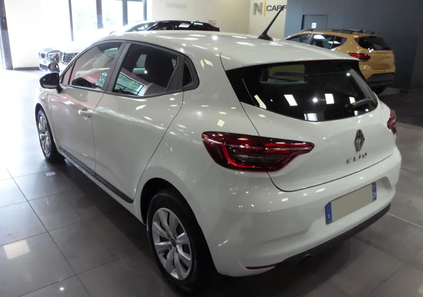 Renault Clio V blanc glacier vue 3/4 arrière droit en intérieur, avec feux arrière LED et jantes alliage.