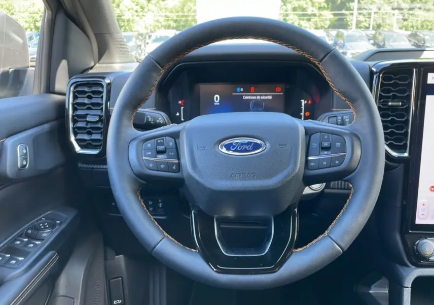 Vue intérieure centrée sur le volant noir à surpiqûres marron du Ford Ranger 2025 gris carbone avec tableau de bord numérique.