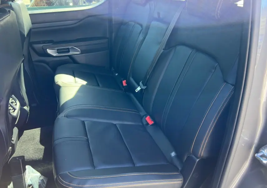 Vue intérieure côté arrière droit du Ford Ranger 2025 gris carbone, sièges en cuir noir avec surpiqûres orange visibles.
