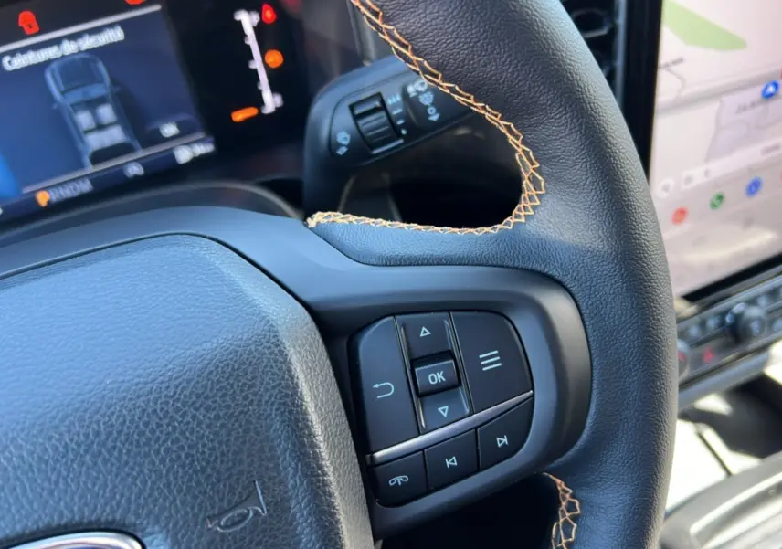 Gros plan sur le volant noir avec surpiqûres orange du Ford Ranger 2025 Wildtrak Plus, tableau de bord et écran tactile visibles.