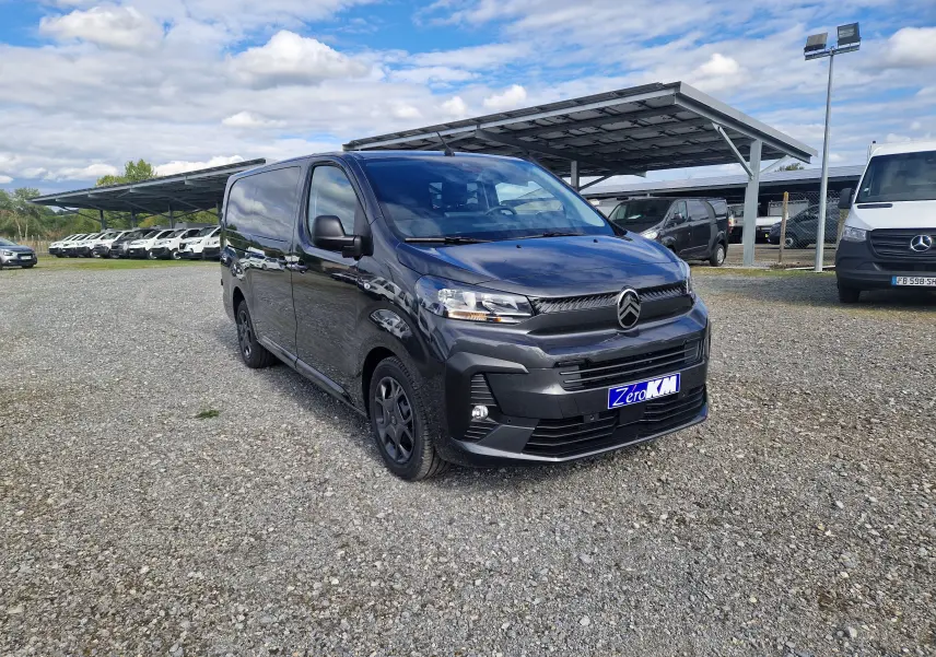 Vue 3/4 avant droit d'un Citroën Jumpy cabine approfondie gris titane avec jantes tôles 17 pouces sur parking gravillonné.