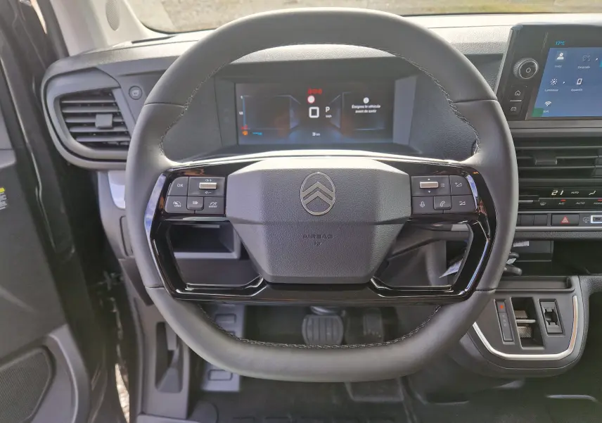 Vue rapprochée du volant cuir noir du Citroën Jumpy XL gris titane, avec tableau de bord numérique et console centrale visible.