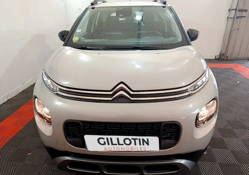 Vue frontale d'un Citroën C3 Aircross blanc avec calandre noire et phares allumés en intérieur showroom.