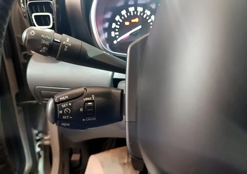 Gros plan sur les commandes de régulateur et feux au volant cuir d'une Citroën C3 Aircross blanche de 2019.