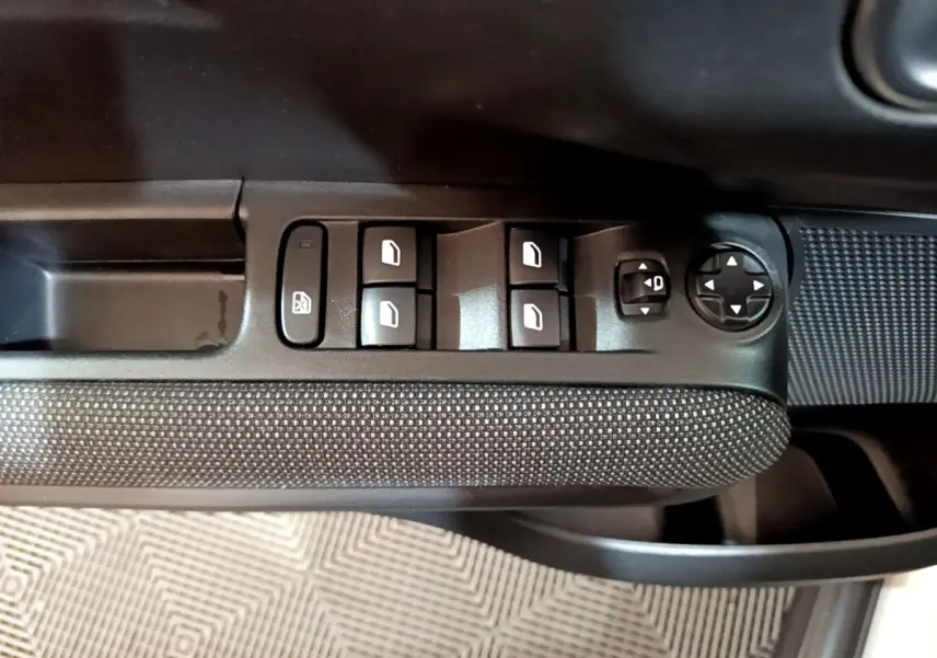 Gros plan sur les commandes de lève-vitres et réglages des rétroviseurs côté conducteur d'une Citroën C3 Aircross blanche.