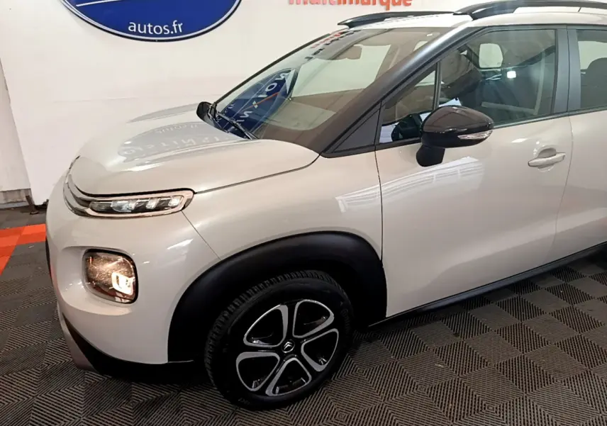 Vue 3/4 avant droit d'un Citroën C3 Aircross blanc avec jantes noires et barres de toit noires.