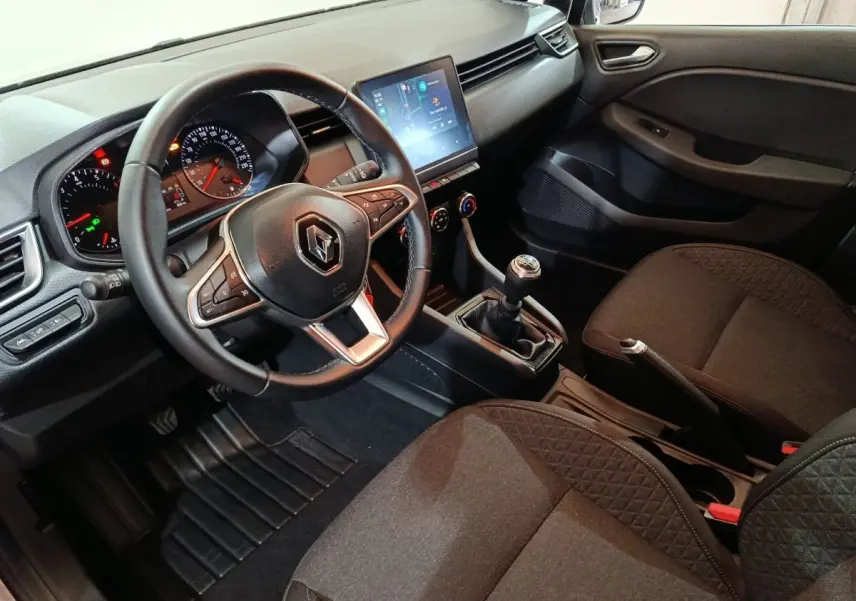 Vue intérieure côté conducteur de la Renault Clio gris clair 2023, volant cuir, écran tactile et boîte manuelle visible.