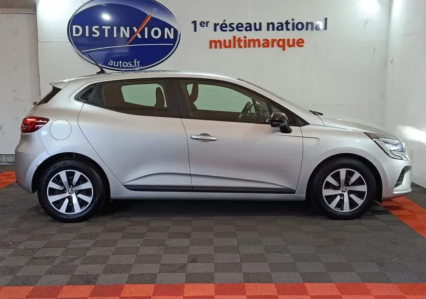 Profil droit d'une Renault Clio gris clair 2023, avec jantes alliage et rétroviseurs noirs dans un showroom.