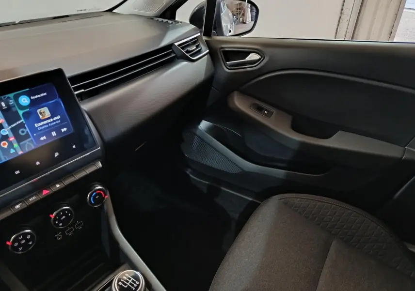 Vue intérieure côté passager de la Renault Clio gris clair 2023, avec écran tactile et console centrale manuelle.