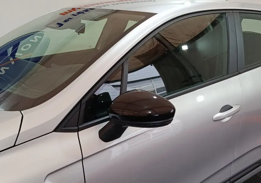 Vue côté gauche rapprochée d’une Renault Clio gris clair 2023 avec rétroviseur noir brillant et poignée de porte visible.