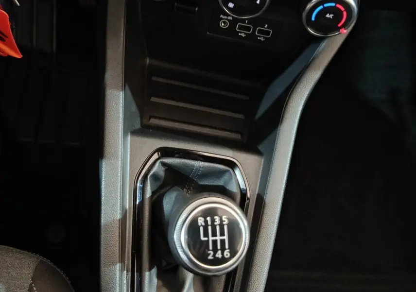 Vue plongeante sur la console centrale d’une Renault Clio gris clair 2023, avec levier de vitesse manuel et commandes de climatisation.