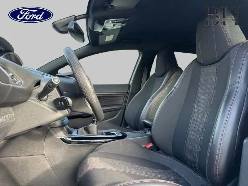 Vue intérieure côté conducteur de la Peugeot 308 SW gris Artense, sièges sport en tissu noir avec surpiqûres rouges.