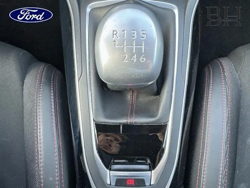 Le levier de vitesses manuel vu de dessus avec coutures rouges sur le soufflet, entouré des sièges sport noirs.
