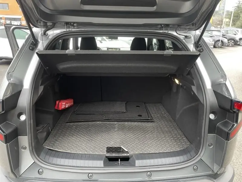 Coffre ouvert vu de l'arrière d'un Dacia Duster 1.6 Hybrid gris schiste 2025, avec tapis de sol et trousse de secours rouge.