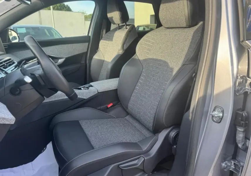 Vue intérieure côté conducteur du Peugeot 3008 Hybrid gris 2025, sièges tissu et cuir bicolore avec console centrale visible.