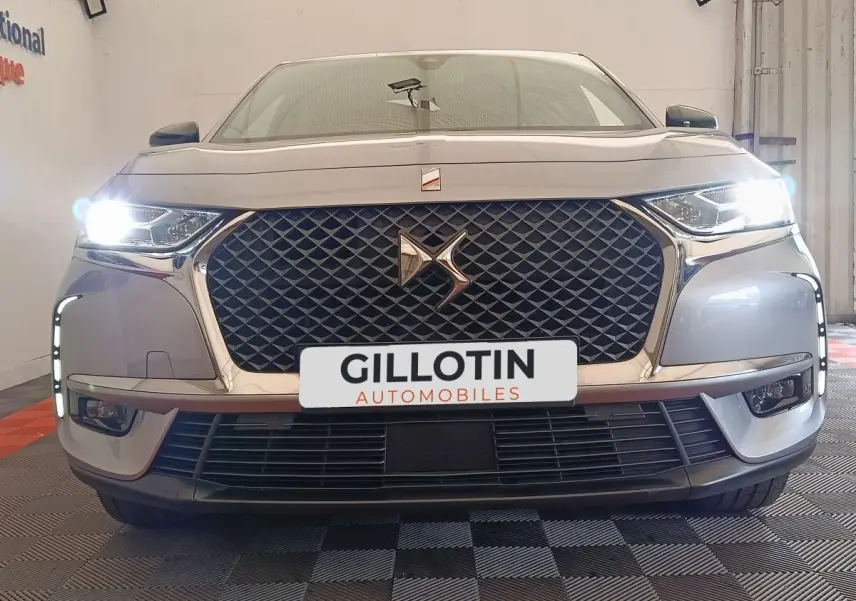 Vue frontale d'un DS7 Crossback E-TENSE gris clair avec phares allumés et calandre distinctive en losanges.