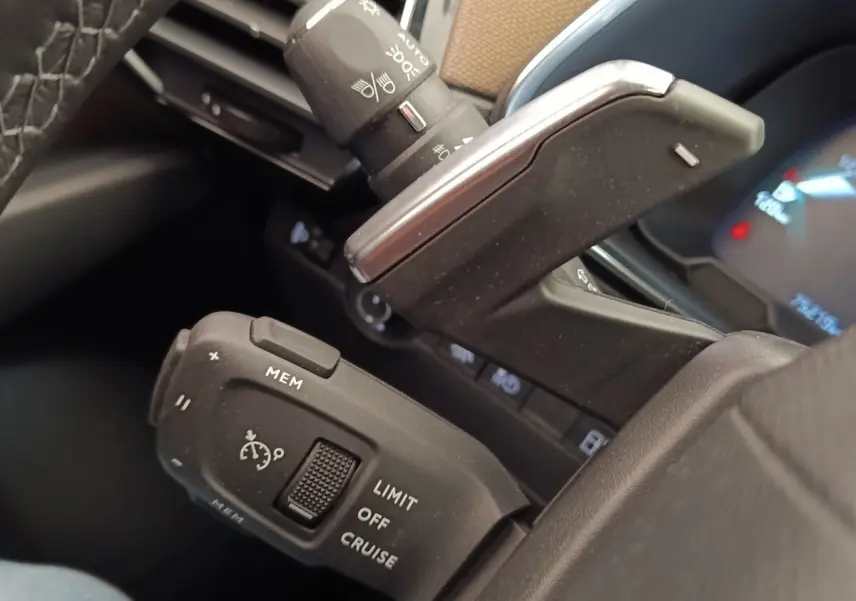 Gros plan sur les commandes au volant cuir noir du DS7 Crossback E-TENSE 225, avec régulateur de vitesse et palettes de boîte auto.