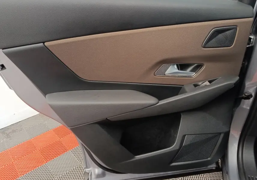 Vue rapprochée de la porte avant droite du DS7 Crossback gris clair, avec habillage marron et noir et poignée argentée.