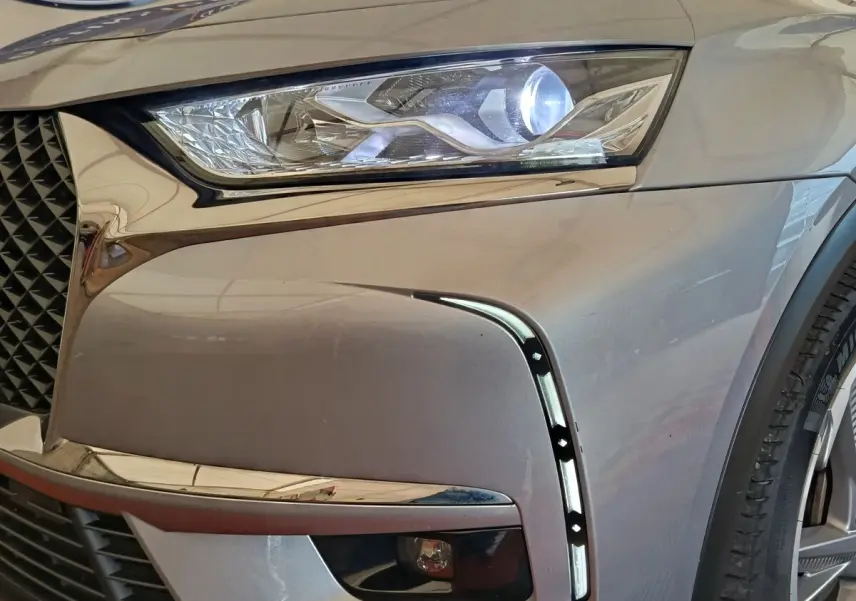 Gros plan sur l'avant droit gris clair du DS7 Crossback E-TENSE 225 avec phare LED allumé et signature lumineuse verticale.