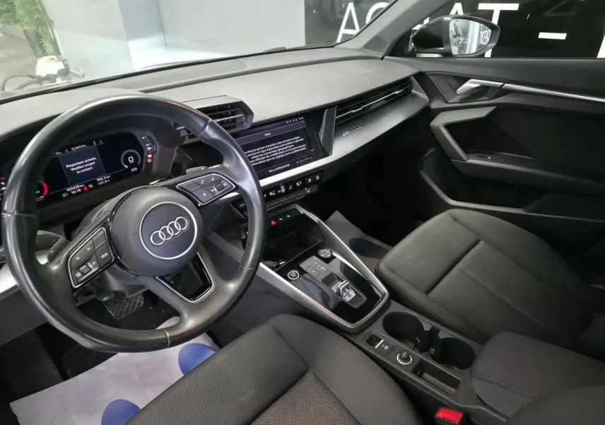 Vue intérieure côté conducteur de l'Audi A3 Sportback 2023 avec tableau de bord digital et sellerie tissu noire.