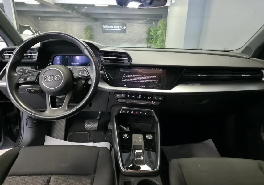 Vue intérieure avant de l'Audi A3 Sportback 2023, tableau de bord noir avec écran digital et volant cuir multifonctions.