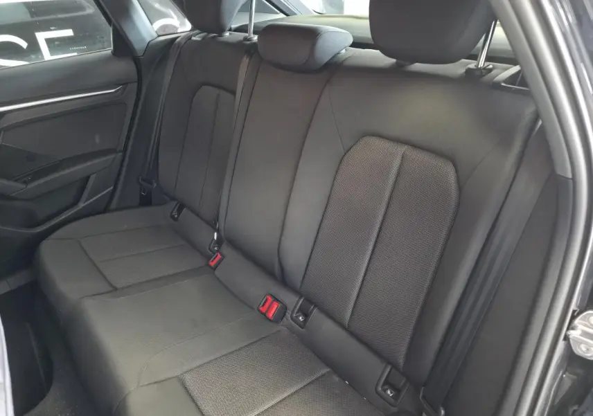 Vue intérieure côté arrière droit de la banquette tissu noire de l'Audi A3 Sportback 2023 avec appuie-têtes et ceintures visibles.
