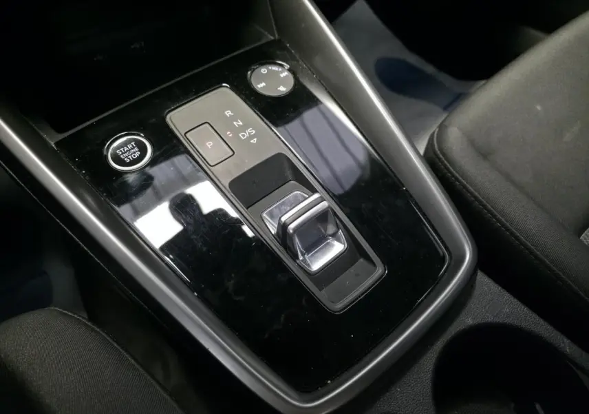 Vue rapprochée de la console centrale noire brillante de l’Audi A3 Sportback 2023 avec sélecteur de boîte auto et bouton start/stop.