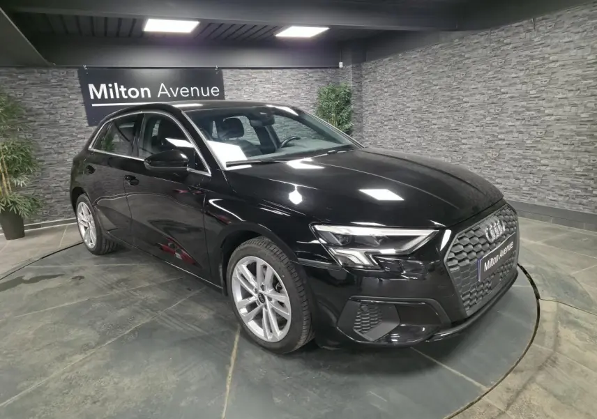 Audi A3 Sportback noir vue 3/4 avant droit en intérieur avec calandre noire et jantes alliage 17 pouces.