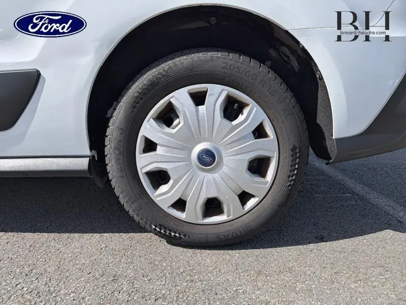 Gros plan sur la roue avant droite d’un Ford Transit Connect blanc glacier avec enjoliveur d’origine et logo Ford au centre.