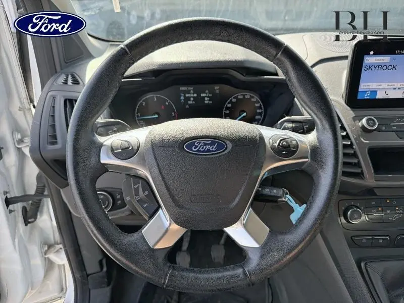 Vue intérieure centrée sur le volant multifonction noir du Ford Transit Connect blanc glacier avec tableau de bord et écran tactile.