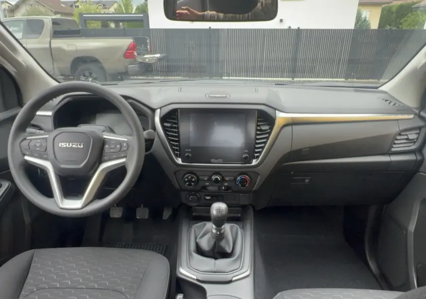 Vue intérieure avant de l'Isuzu D-MAX 2026 avec tableau de bord noir, volant multifonctions et écran tactile central.