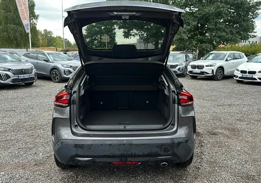 Vue arrière d'une Citroën C4 gris métallisé 2024 avec coffre ouvert sur un parking extérieur.