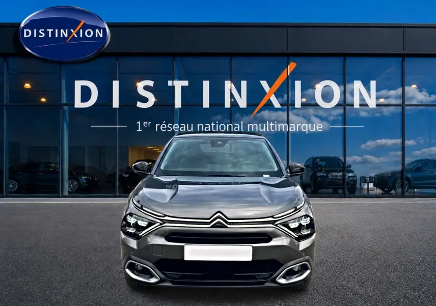 Citroën C4 gris 2024 vue de face, avec phares LED et calandre distinctive devant un showroom Distinxion.