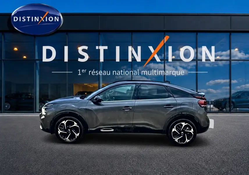 Profil côté gauche d'une Citroën C4 gris 2024 avec jantes alu noires et toit noir devant un bâtiment Distinxion.