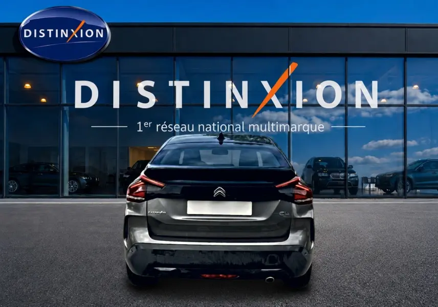 Vue arrière d'une Citroën C4 gris métallisé 2024, stationnée devant une vitrine avec logo Distinxion.