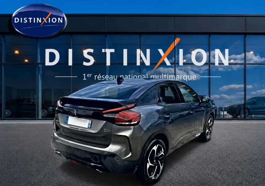 Vue 3/4 arrière droite d'une Citroën C4 gris métallisé avec jantes alu, devant une vitrine Distinxion.