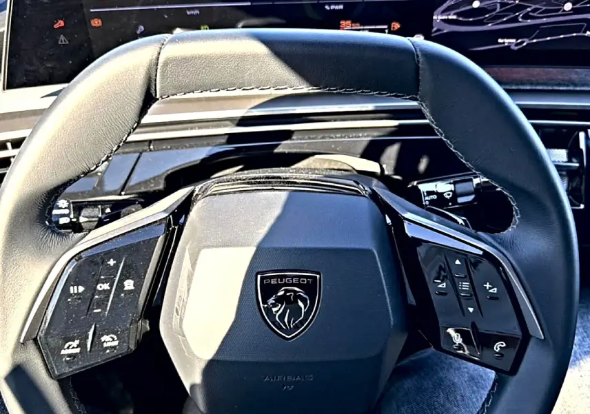 Vue rapprochée du volant cuir noir multifonction du Peugeot 3008 1.2 hybrid 145 allure e-dcs6 avec logo lion central.