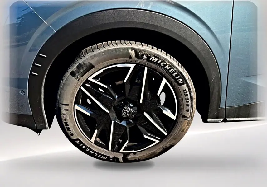 Gros plan sur la roue arrière droite du Peugeot 3008 bleu 2025 avec jante alliage noire et logo Peugeot central.