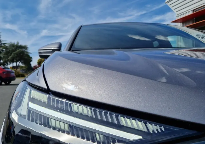 Gros plan sur le phare avant gauche de l'Audi Q4 E-TRON SPORTBACK gris thyphon sous un ciel bleu lumineux.