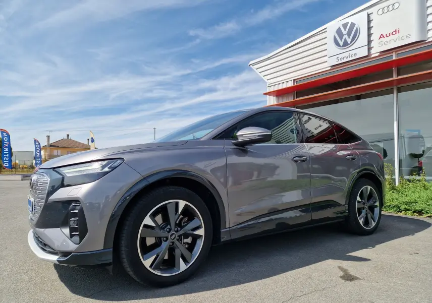 Audi Q4 E-TRON Sportback gris thyphon vue 3/4 avant droit, soulignant ses jantes modernes et sa silhouette électrique élégante.