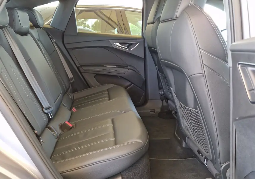 Intérieur arrière de l'Audi Q4 E-TRON SPORTBACK gris thyphon, vue côté gauche avec sièges en cuir noir et toit ouvrant.