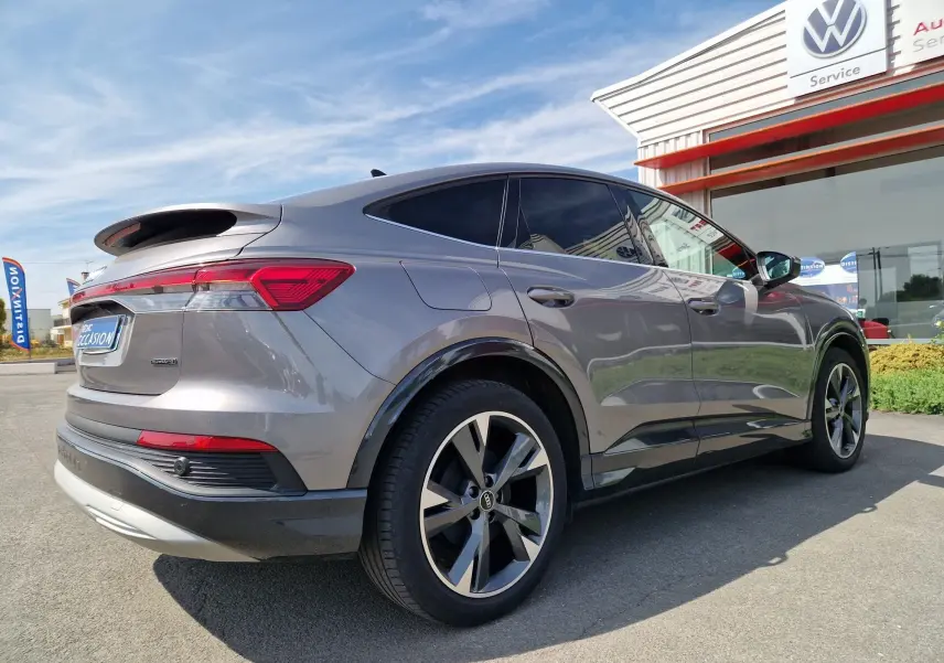 Audi Q4 E-TRON Sportback gris thyphon vu en 3/4 arrière droit, soulignant ses lignes fluides et ses jantes modernes.