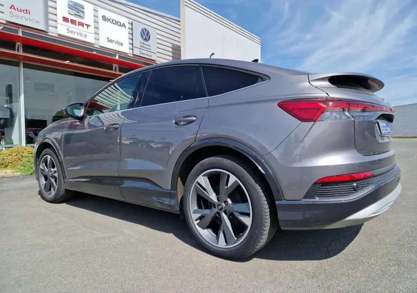 Audi Q4 E-TRON Sportback gris thyphon vu de 3/4 arrière droit, soulignant ses lignes fluides et ses jantes modernes.