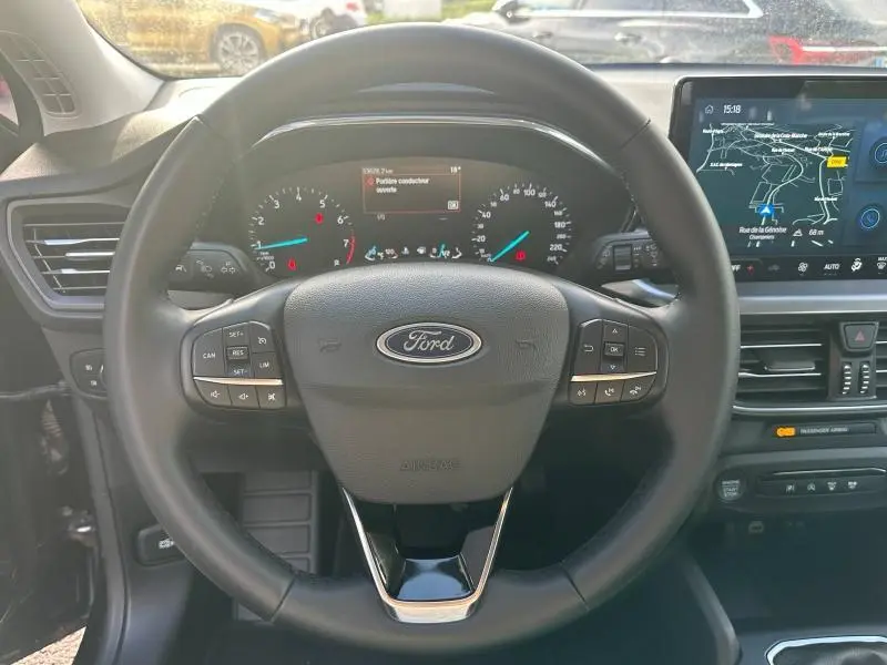 Vue rapprochée du volant cuir multifonction d'une Ford Focus 2023, avec tableau de bord et écran tactile GPS visibles.