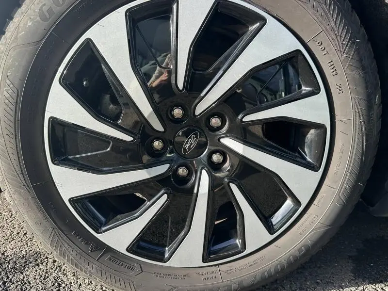 Gros plan sur une jante alliage bicolore noire et argentée avec logo Ford, montée sur une Ford Focus noire Agate 2023.