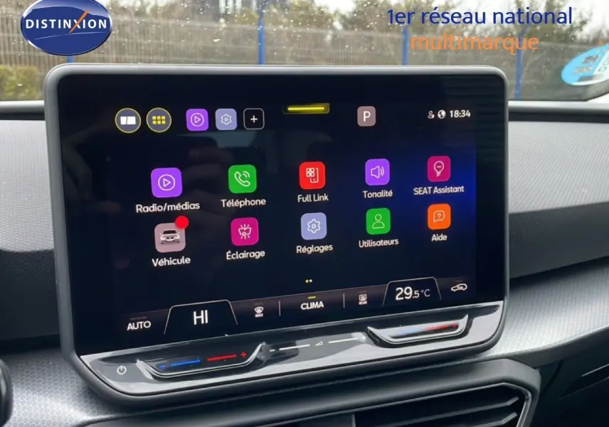 Vue intérieure centrée sur l'écran tactile du tableau de bord du SEAT LEON ST bleu Fjord, affichant les options multimédia et climatisation.