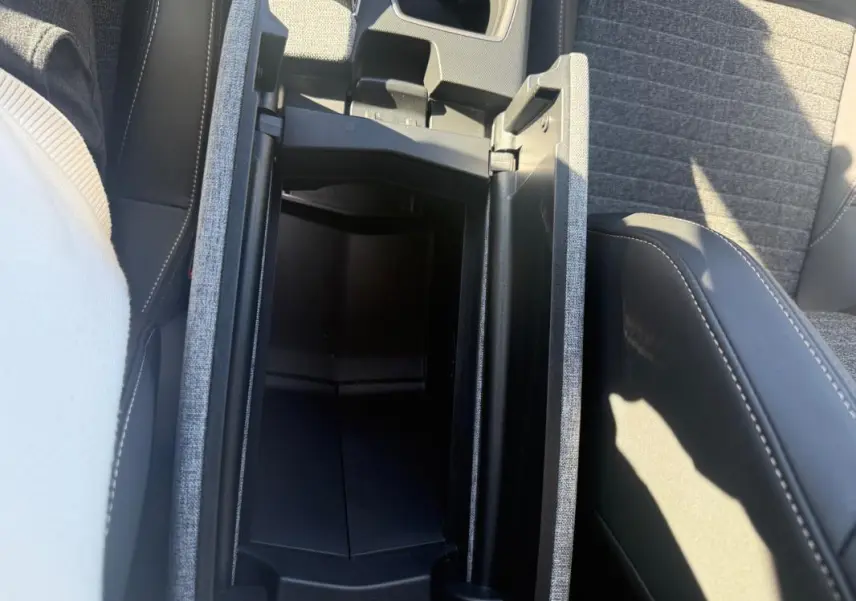 Vue plongeante sur la console centrale ouverte du Peugeot 3008 Hybrid gris, montrant le rangement intérieur et les sièges tissu.